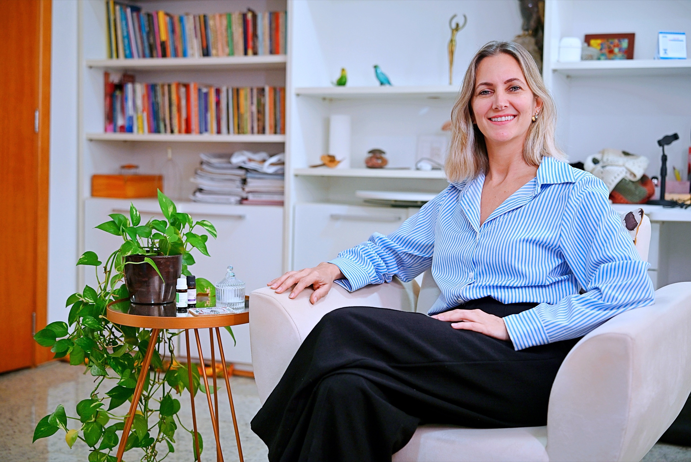 Debora Campana na foto de capa do Método Corpo Regulador, sentada à direita em seu consultório e olhando para a câmera.